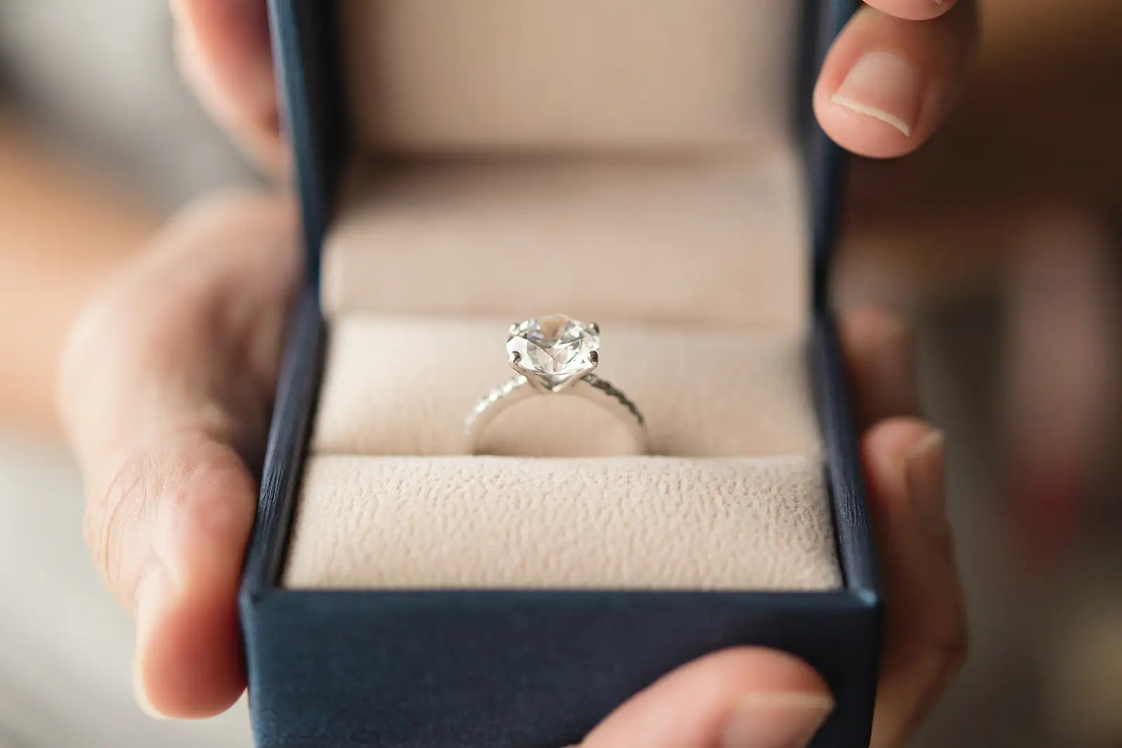 Woman’s hand holding a blue gift box with a diamond ring from Joe Kassab Jewelers