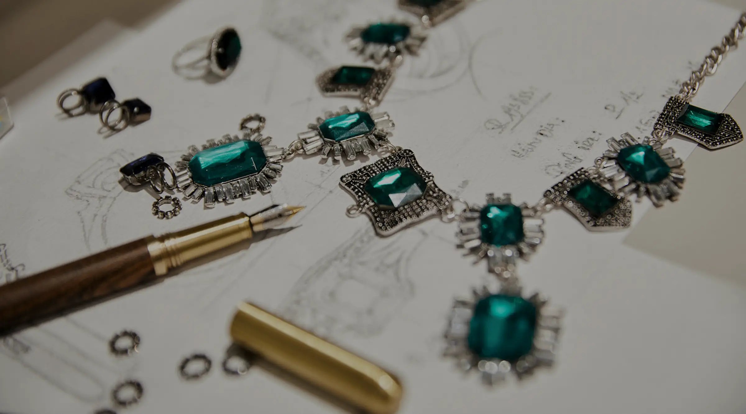 Emerald gemstones next to pen and custom jewelry design plans at Joe Kassab Jewelers